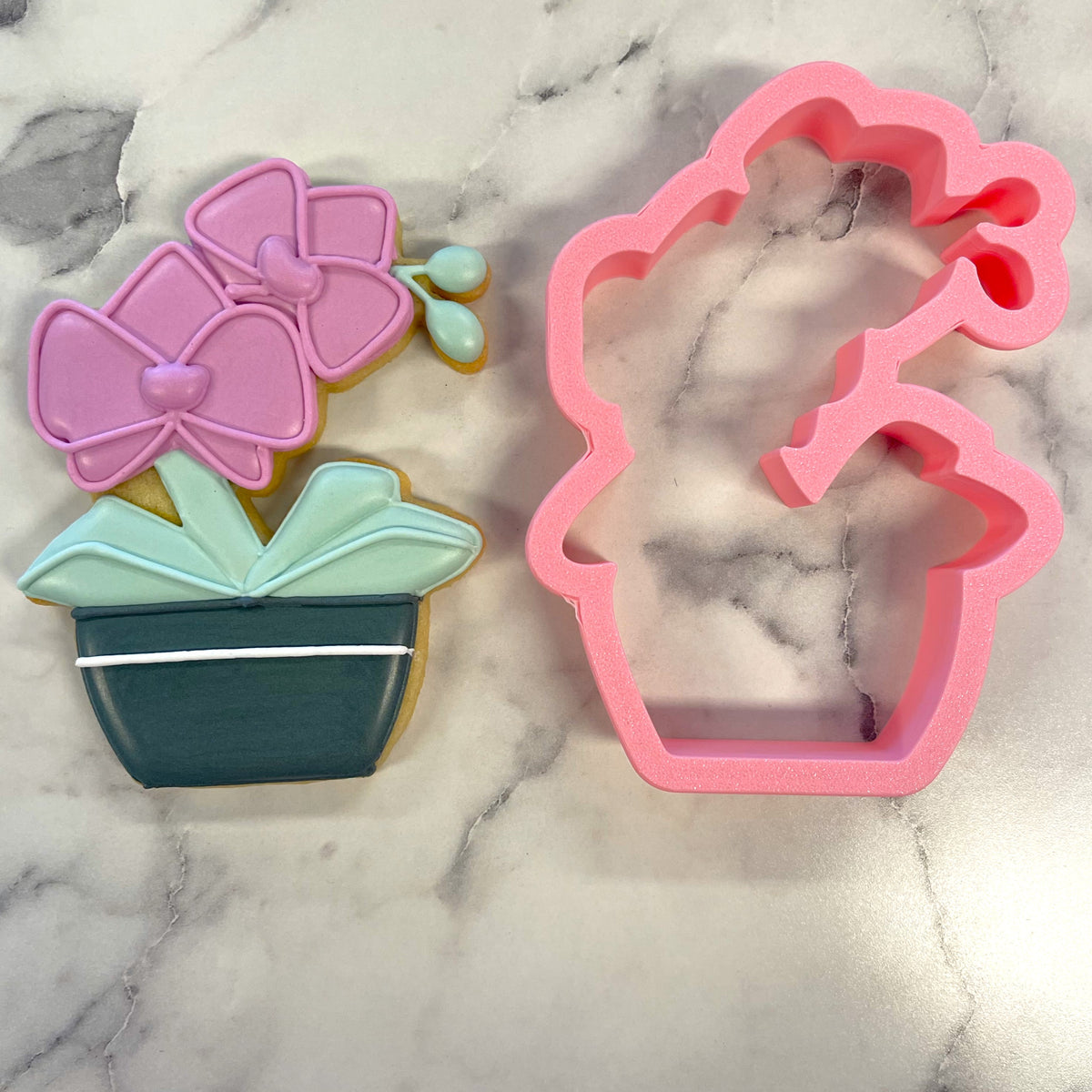 Pink silicone orchid cookie cutter next to a decorated orchid-shaped cookie for baking and decorating use