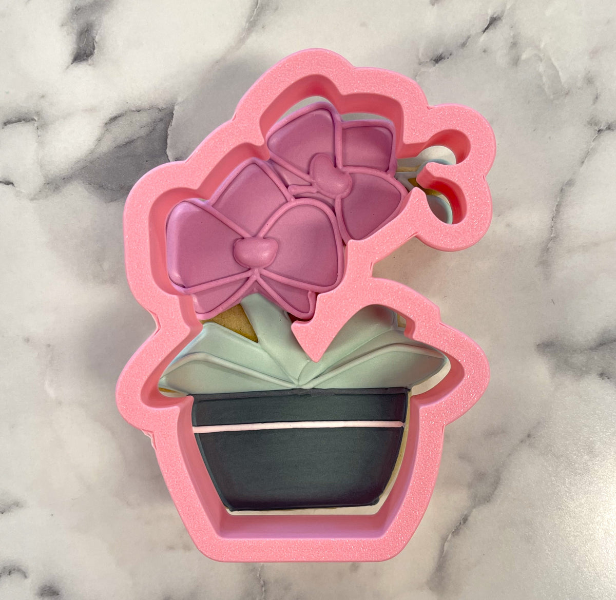 Pink silicone orchid cookie cutter shaped like a potted orchid with a large purple bow for baking