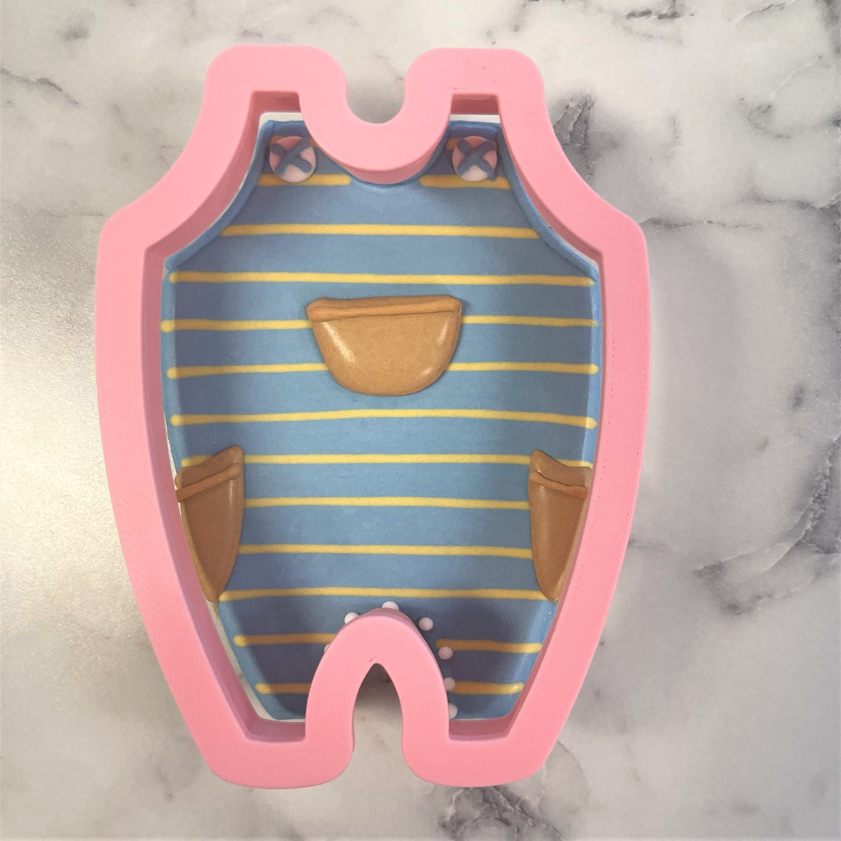 Pink silicone baby overalls cookie cutter with blue yellow stripes brown pocket details and white polka dots