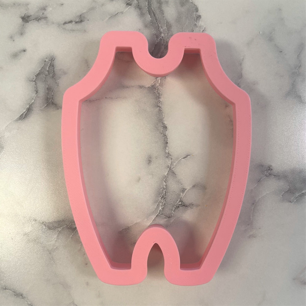 Pink silicone baby overalls cookie cutter shaped like a baby onesie for baking and decorating baby-themed treats