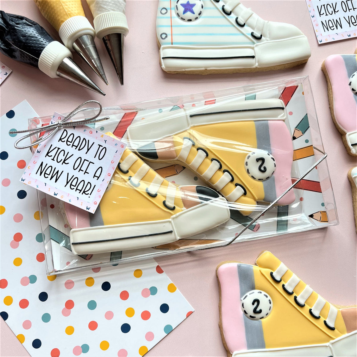 Yellow high-top sneaker shaped cookie in clear plastic gift box with decorative tag for high top sneaker cookie cutter