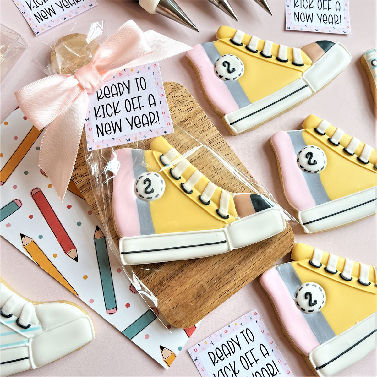 Yellow and pink high top sneaker-shaped cookies with white laces gray stripes and black stitching detail using cookie cutter