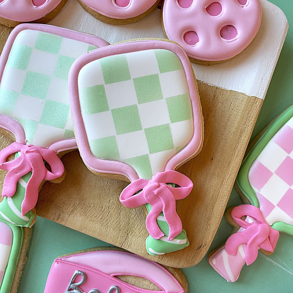 Pastel green and white checkered paddle shaped sugar cookie with pink icing from pickleball preppy cookie cutter bundle