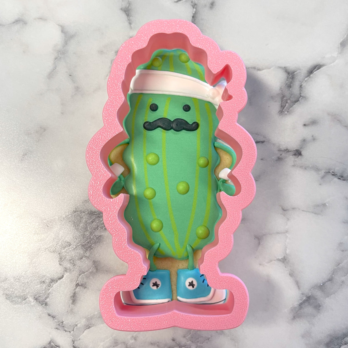 Pickle baller cookie cutter shaped like green cactus figurine with mustache white headband and blue sneakers