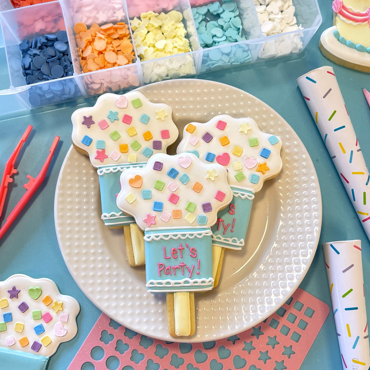 Three colorful candy-coated ice cream pop cookie decorations with pastel blue bases and white icing tops with sprinkles