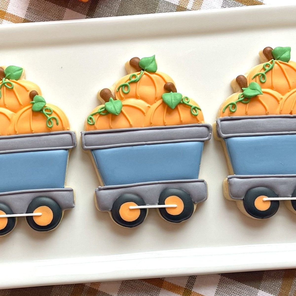 Orange pumpkin-shaped cookies with green leaves and vines in a blue wagon design from pumpkin train cookie cutter bundle