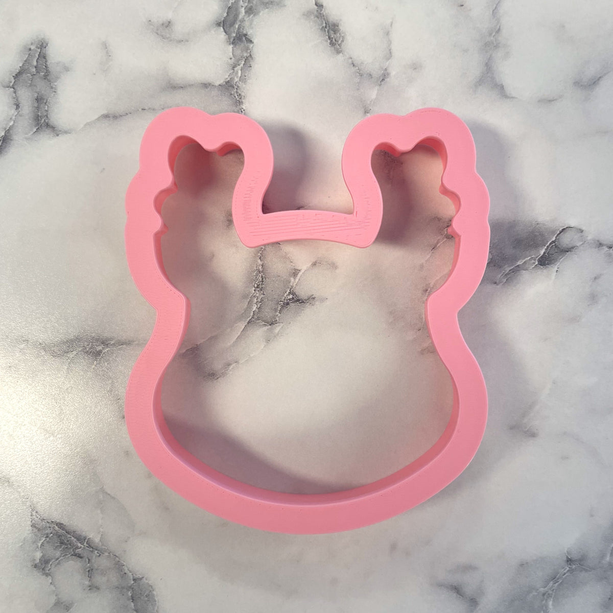 Pink plastic cookie cutter shaped like a bunny with rounded ears for cute reindeer face cookies
