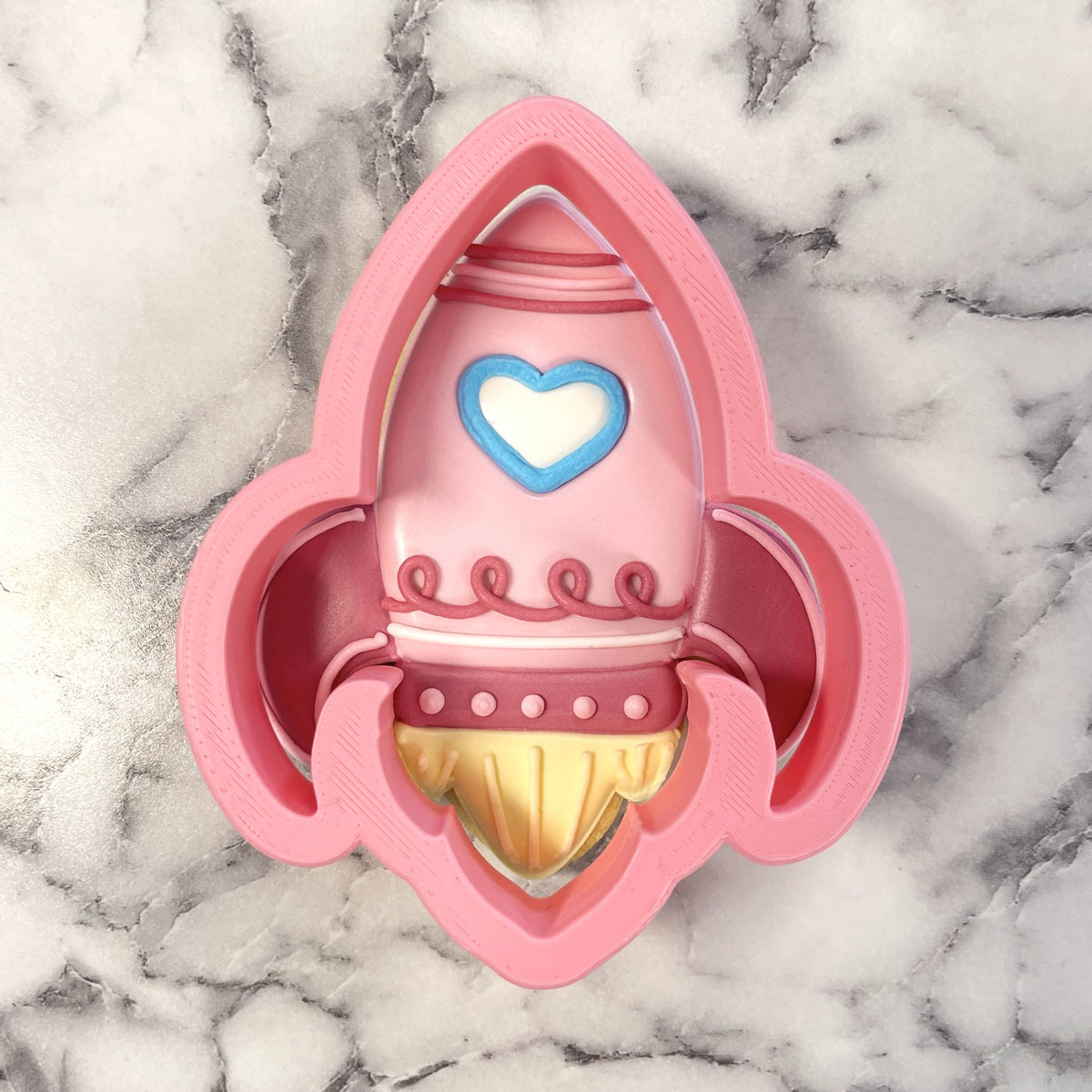 Rocket valentine cookie cutter in pink with a blue heart detail and gold accents for festive baking