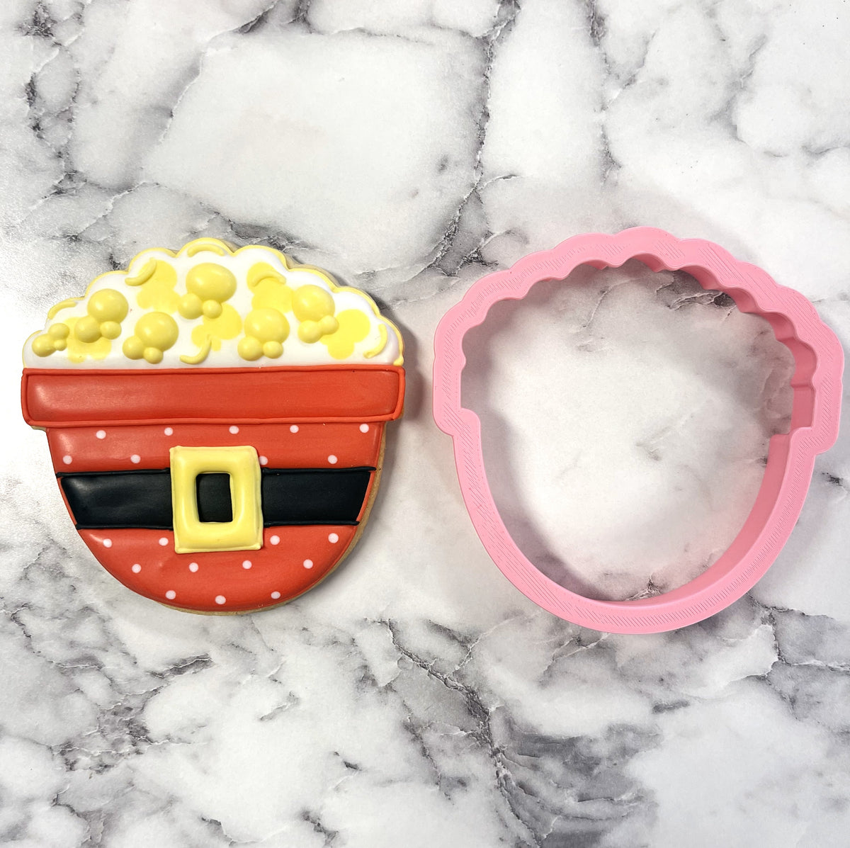 A pink silicone santa popcorn bowl cookie cutter with scalloped edges shaped like a popcorn bucket