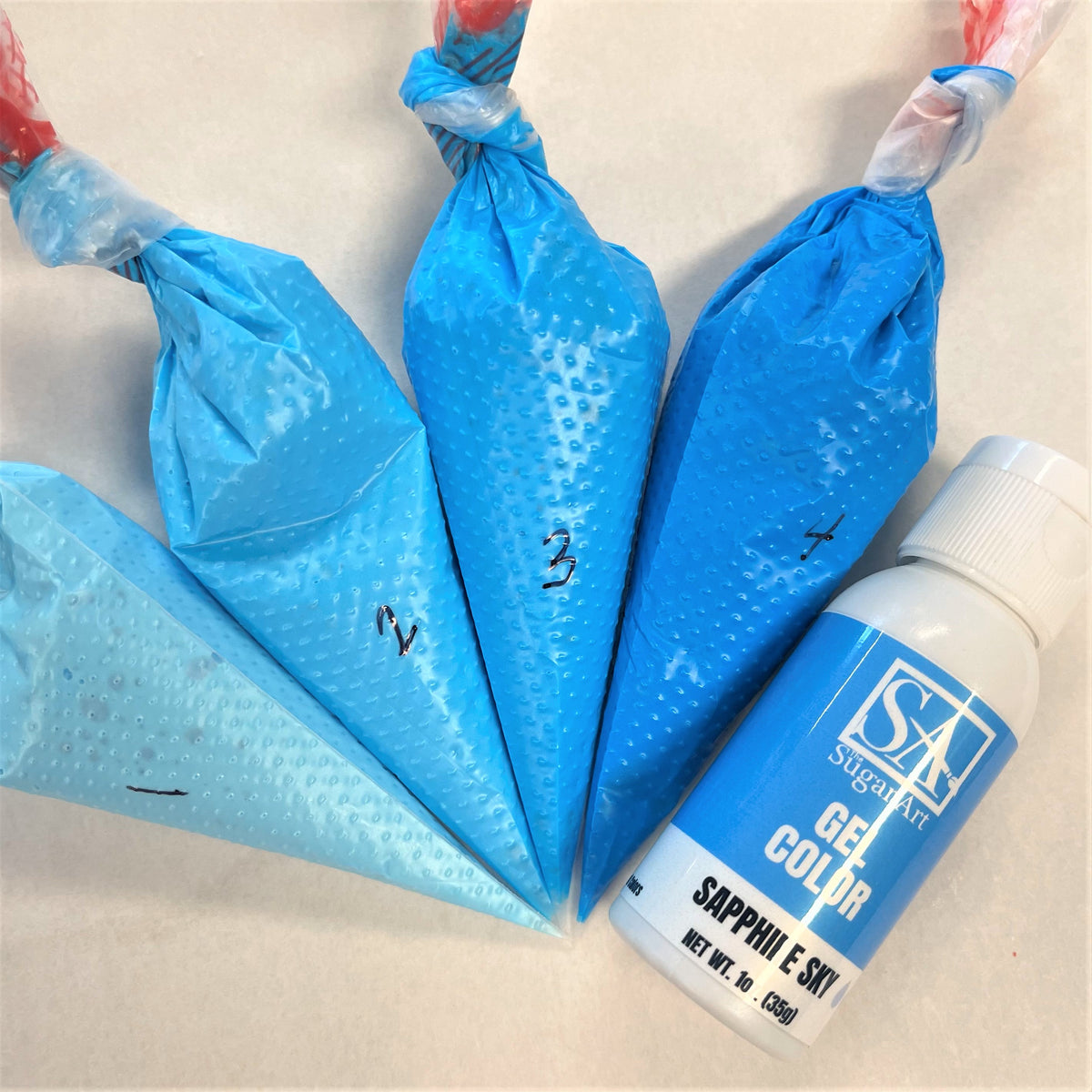 Blue silicone piping bags with numbered markings and a bottle of sapphire sky sugarart gel color for cake decorating