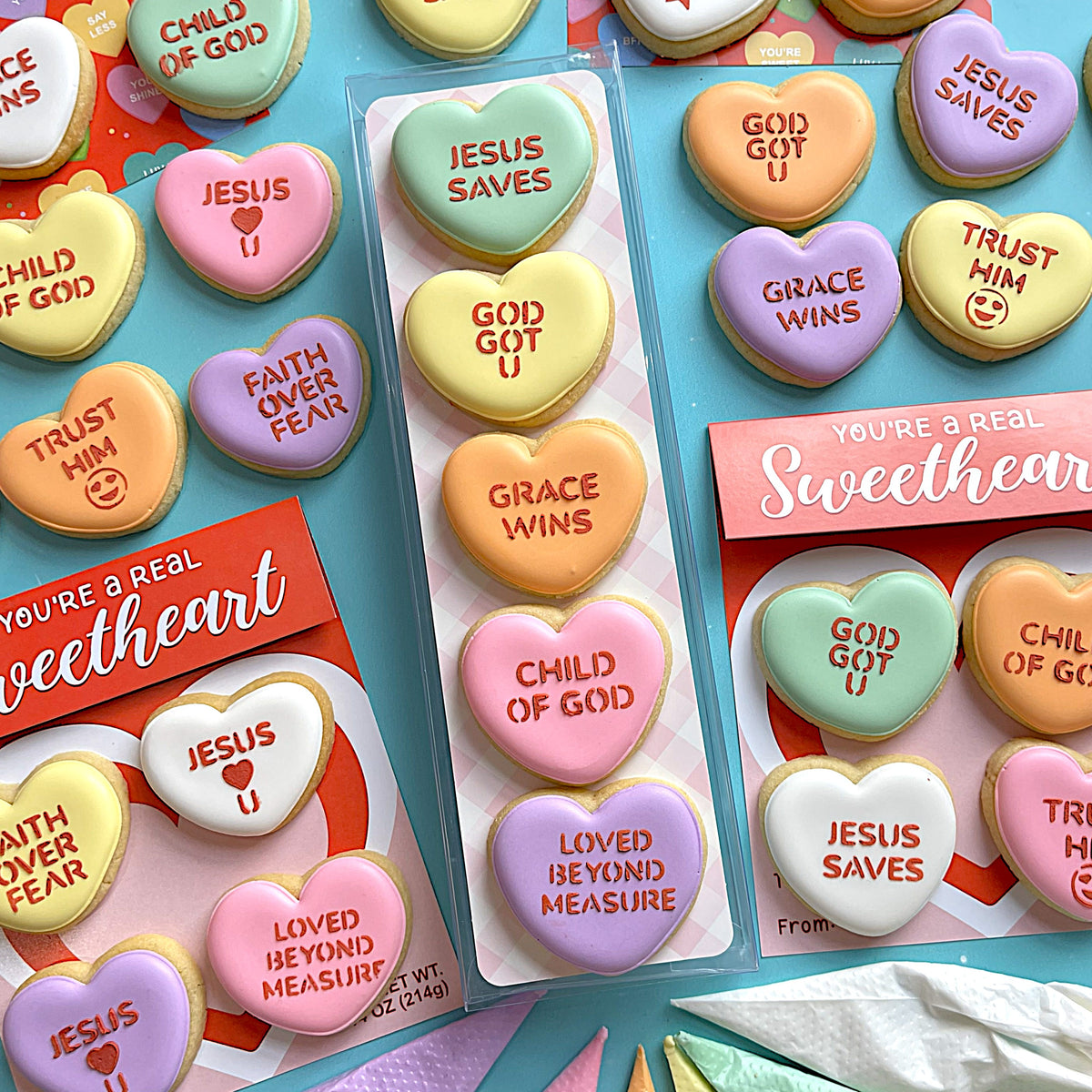 Pastel-colored heart-shaped cookies with faith messages in clear plastic trays for faith conversation heart stencil use
