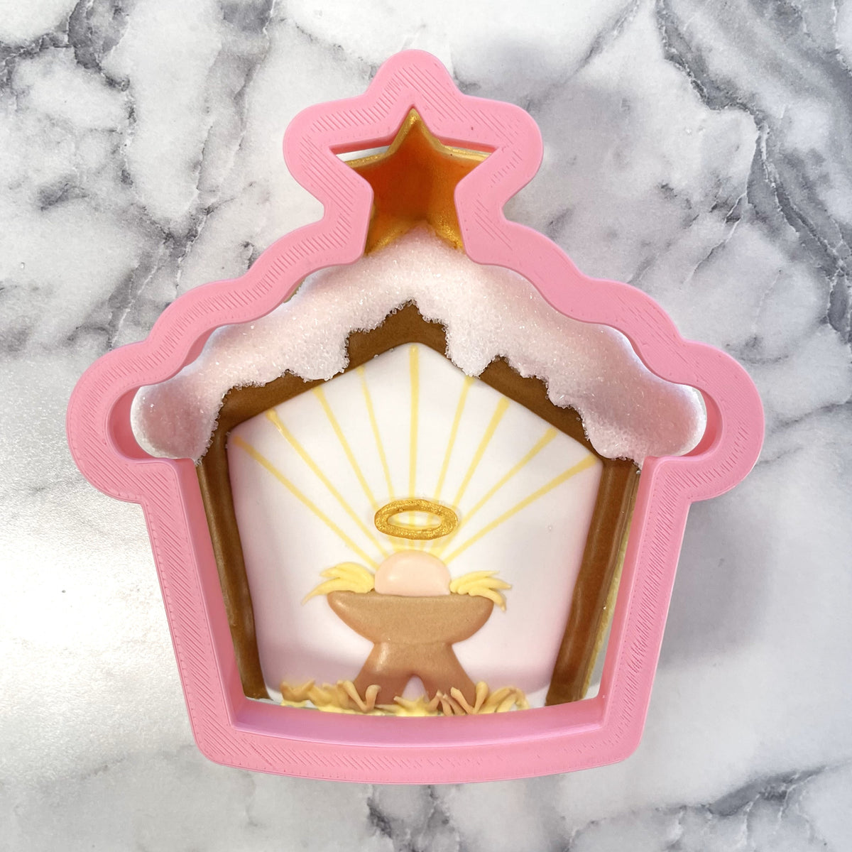 Pink plastic snowy stable cookie cutter shaped like a nativity stable with a golden star on top