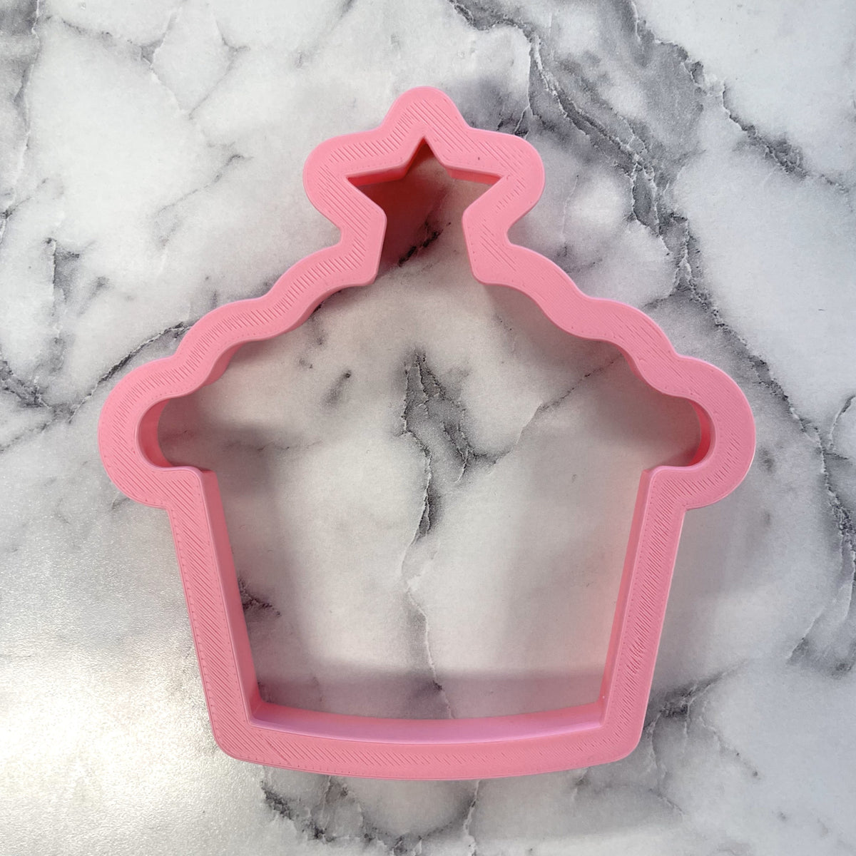 Pink plastic snowy stable cookie cutter shaped like cupcake with star for festive baking and decorating