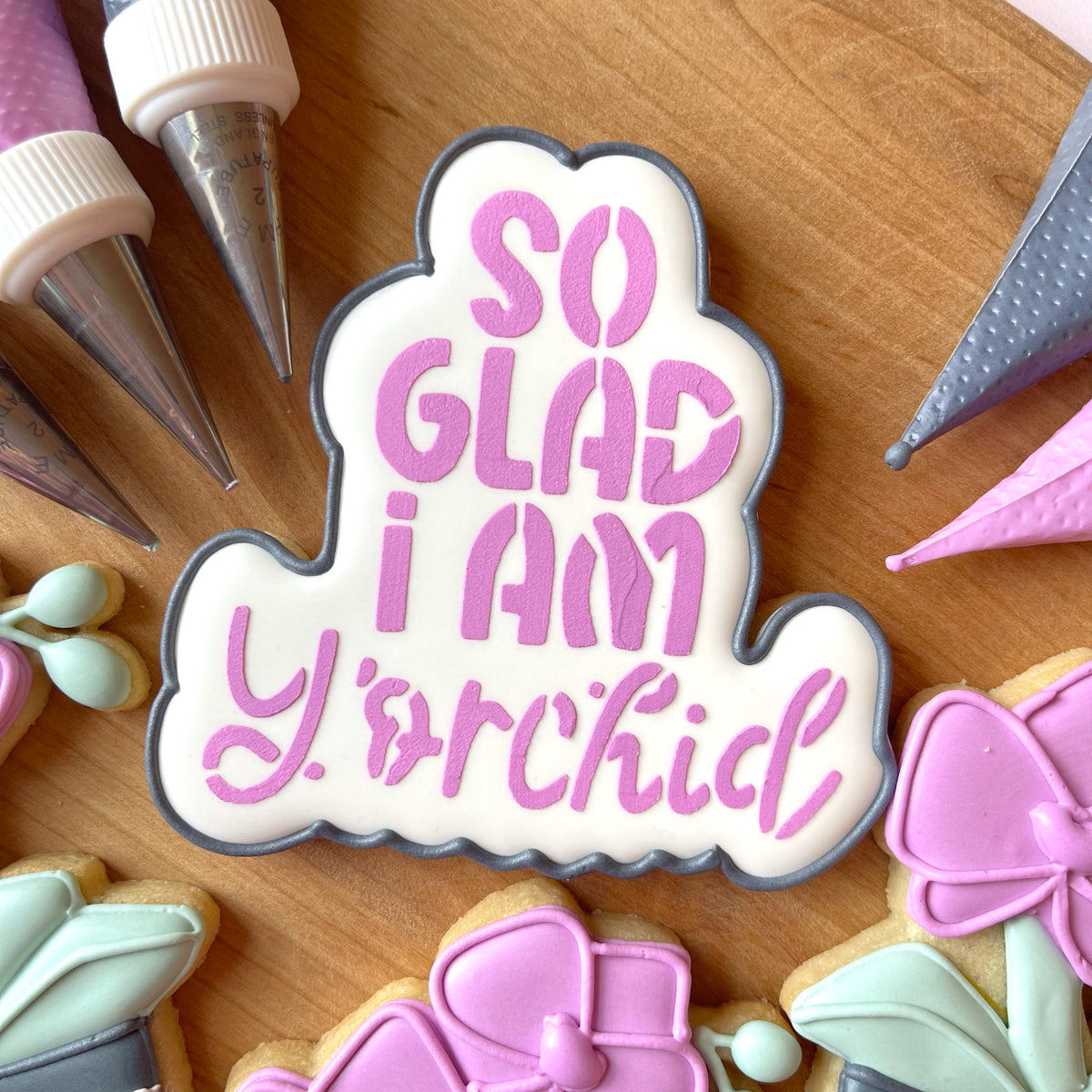 A white frosted cookie with gray border and pink orchid icing from the orchid cookie cutter bundle with stencil