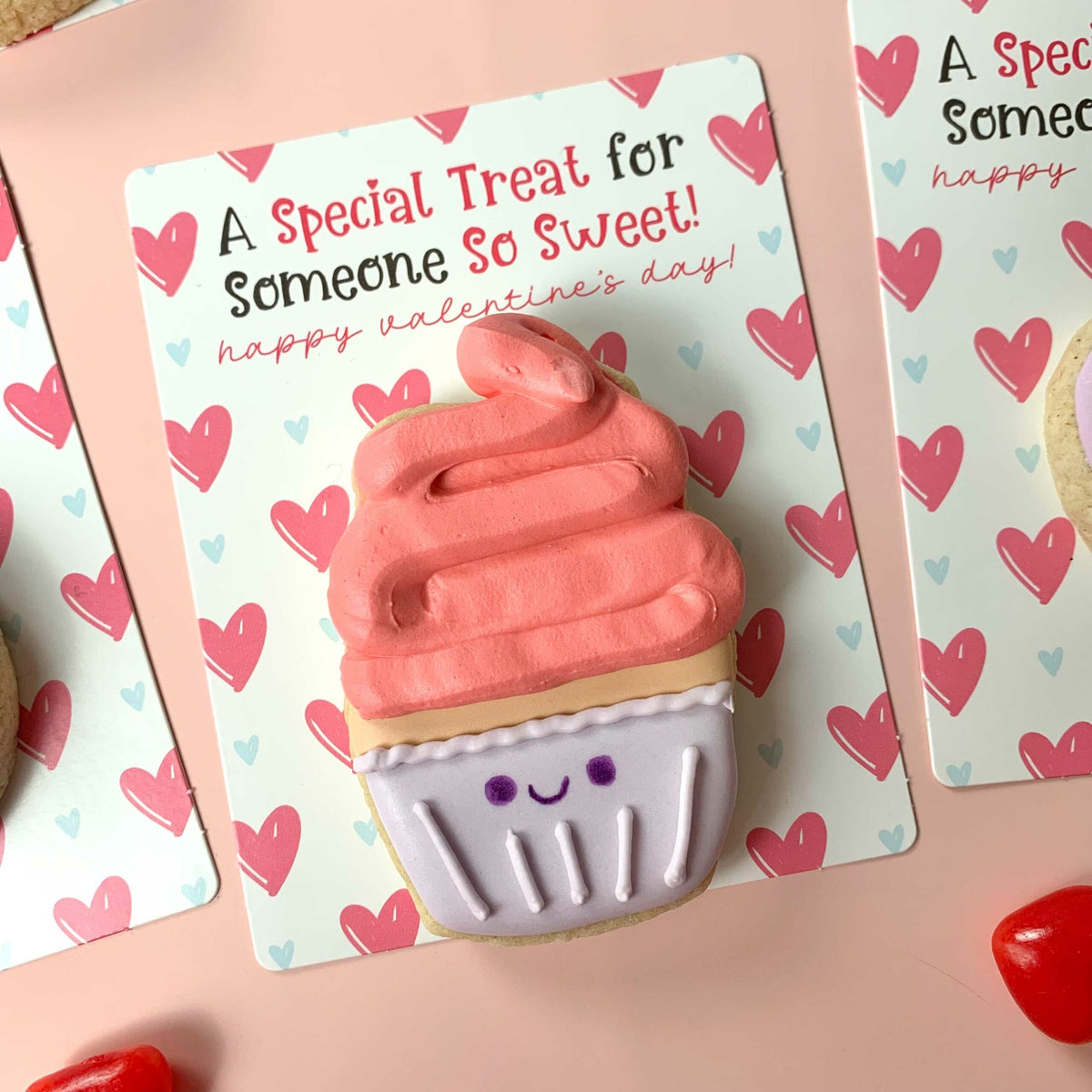 A pink-frosted cupcake-shaped cookie with a smiling face in a lavender paper wrapper on a special treat someone sweet bag backer card