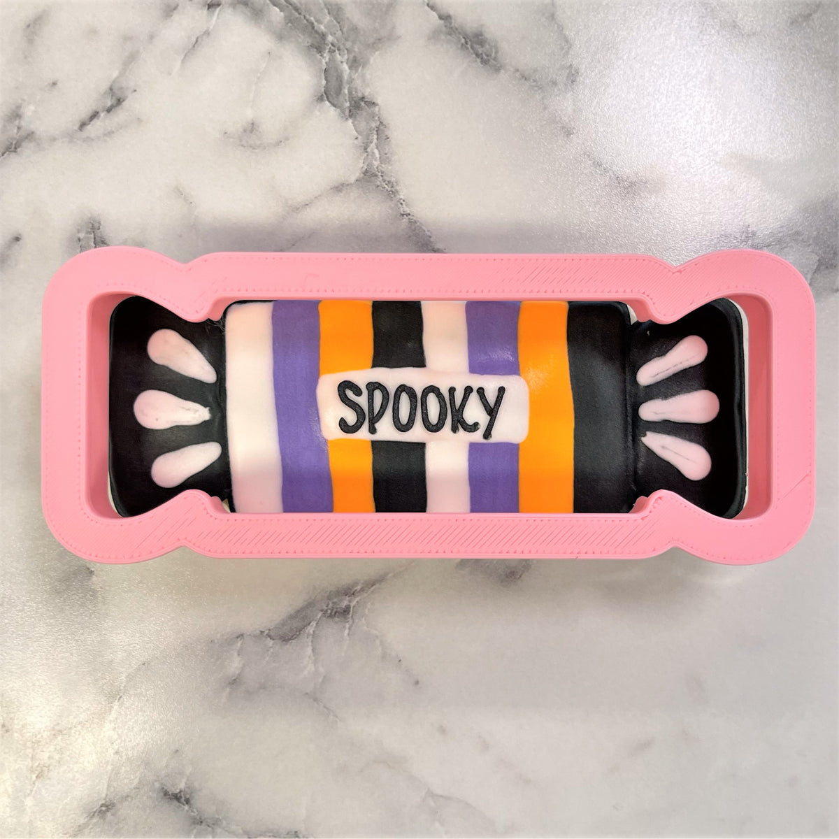 Pink candy-shaped silicone mold with black purple orange and white striped interior featuring the word spooky