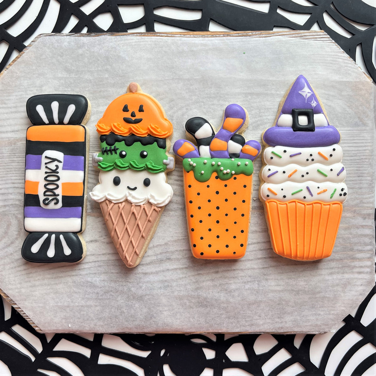Halloween-themed sugar cookies shaped like wrapped long candies ice cream cones and a witch hat next to an orange bucket