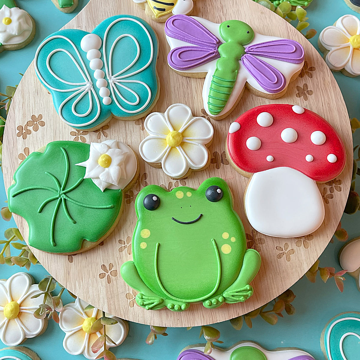 A cheerful green frog-shaped cookie with yellow spots and black eyes made using mushroom pumpkin bucket flour box club flip cookie cutter