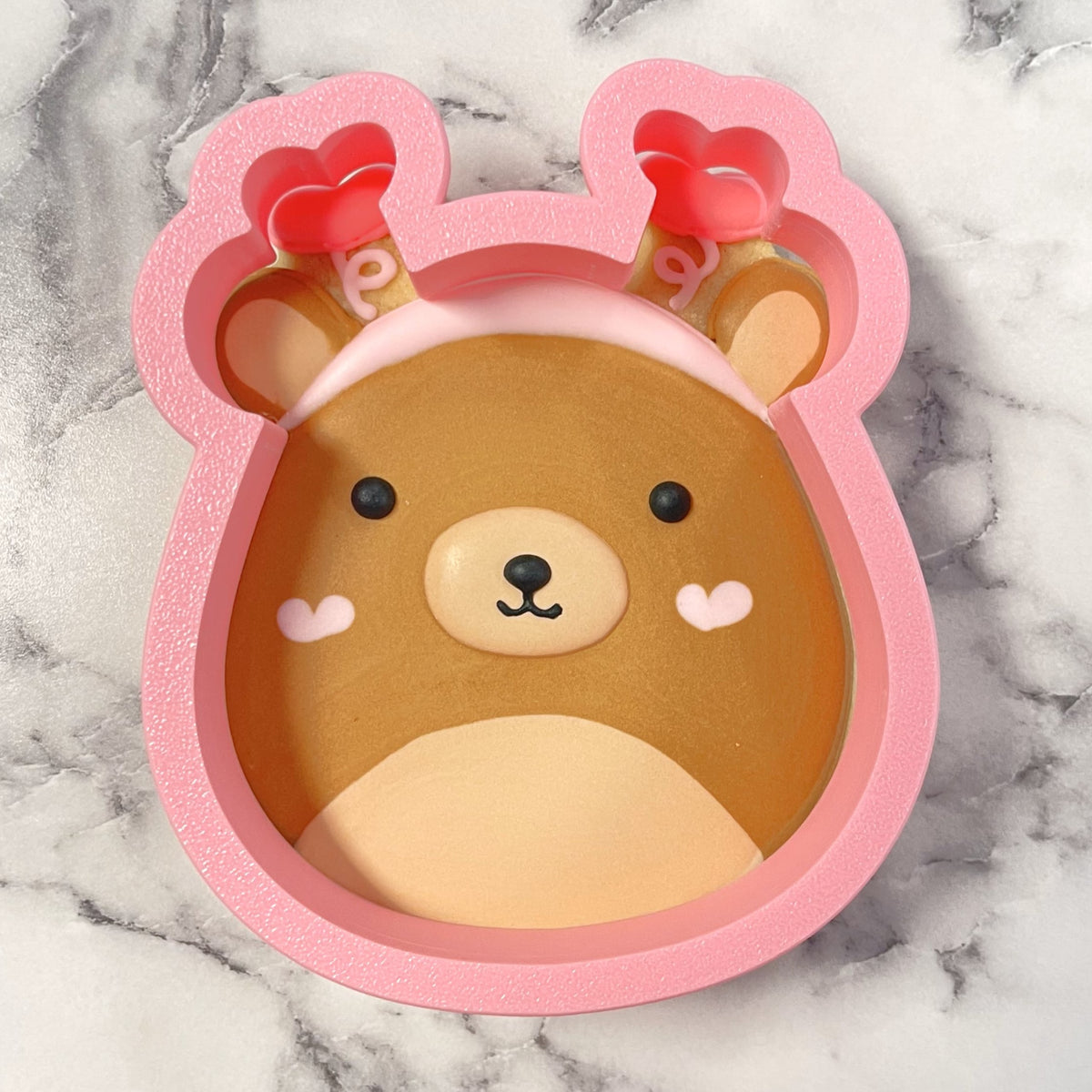 Pink silicone squishie bear cookie cutter with heart-tipped antlers and soft rounded design for baking crafts
