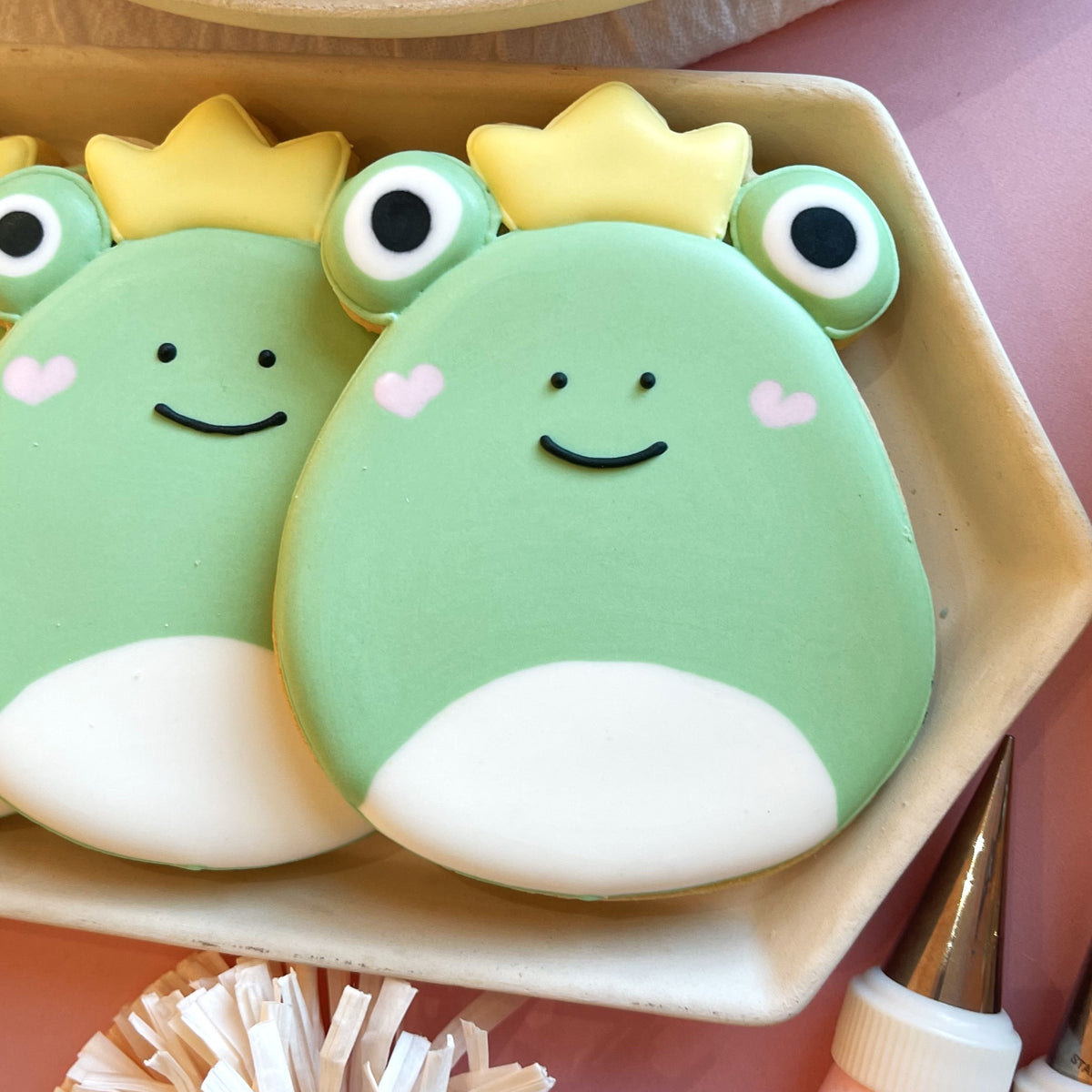 Pastel green frog-shaped cookies with yellow crowns and pink heart cheeks in squishie valentine’s decorating kit