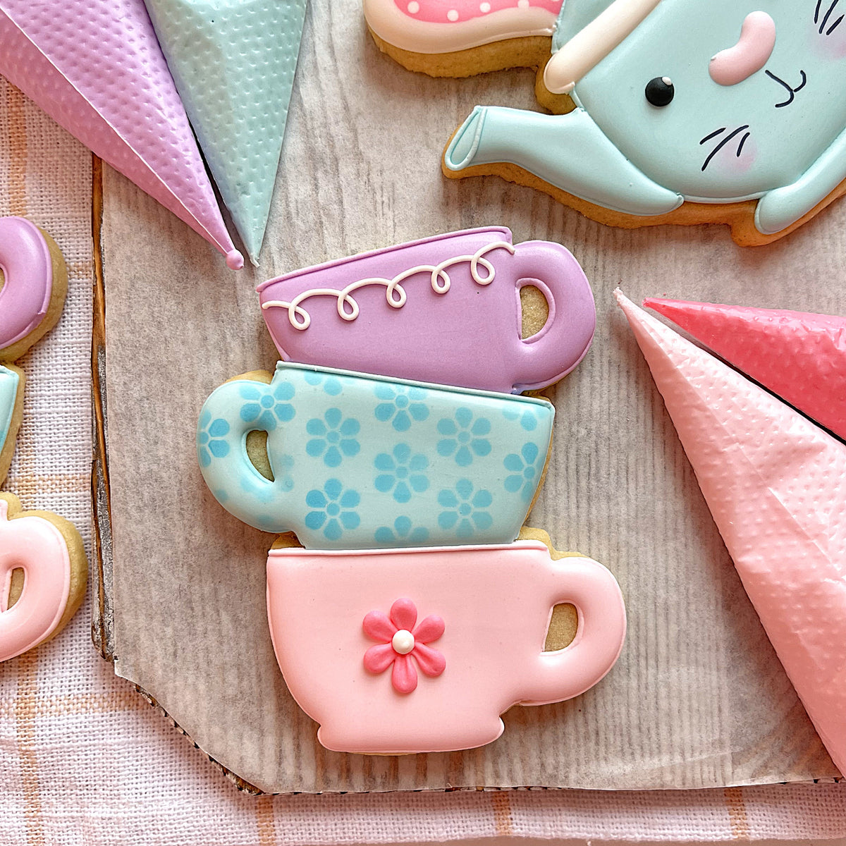 Stacked pastel-colored sugar cookies shaped like teacups with delicate icing and pink flower accents from easter 2025 cookie cutter set