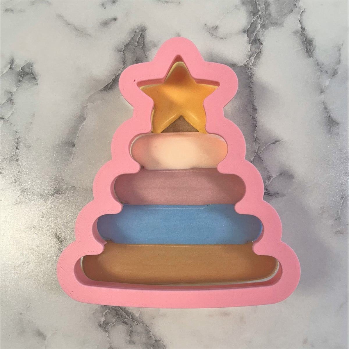 Baby stacking toy cookie cutter made of pink silicone shaped like a christmas tree with tiered pastel rings and golden star