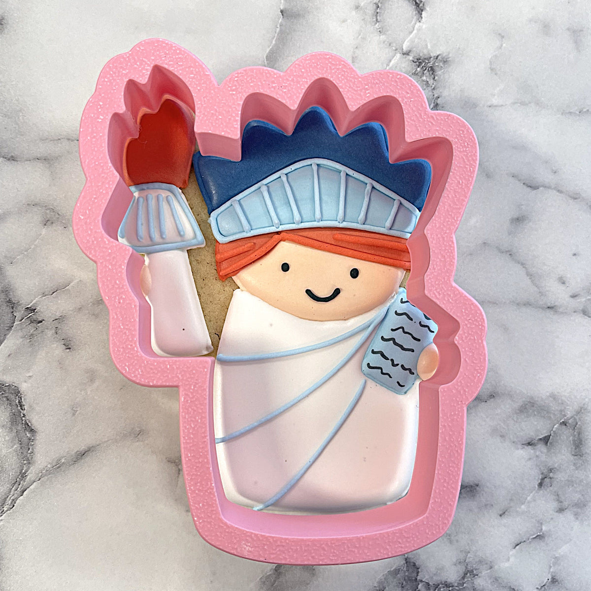 Pink silicone statue of liberty cookie cutter with cartoonish blue crown and orange headband design