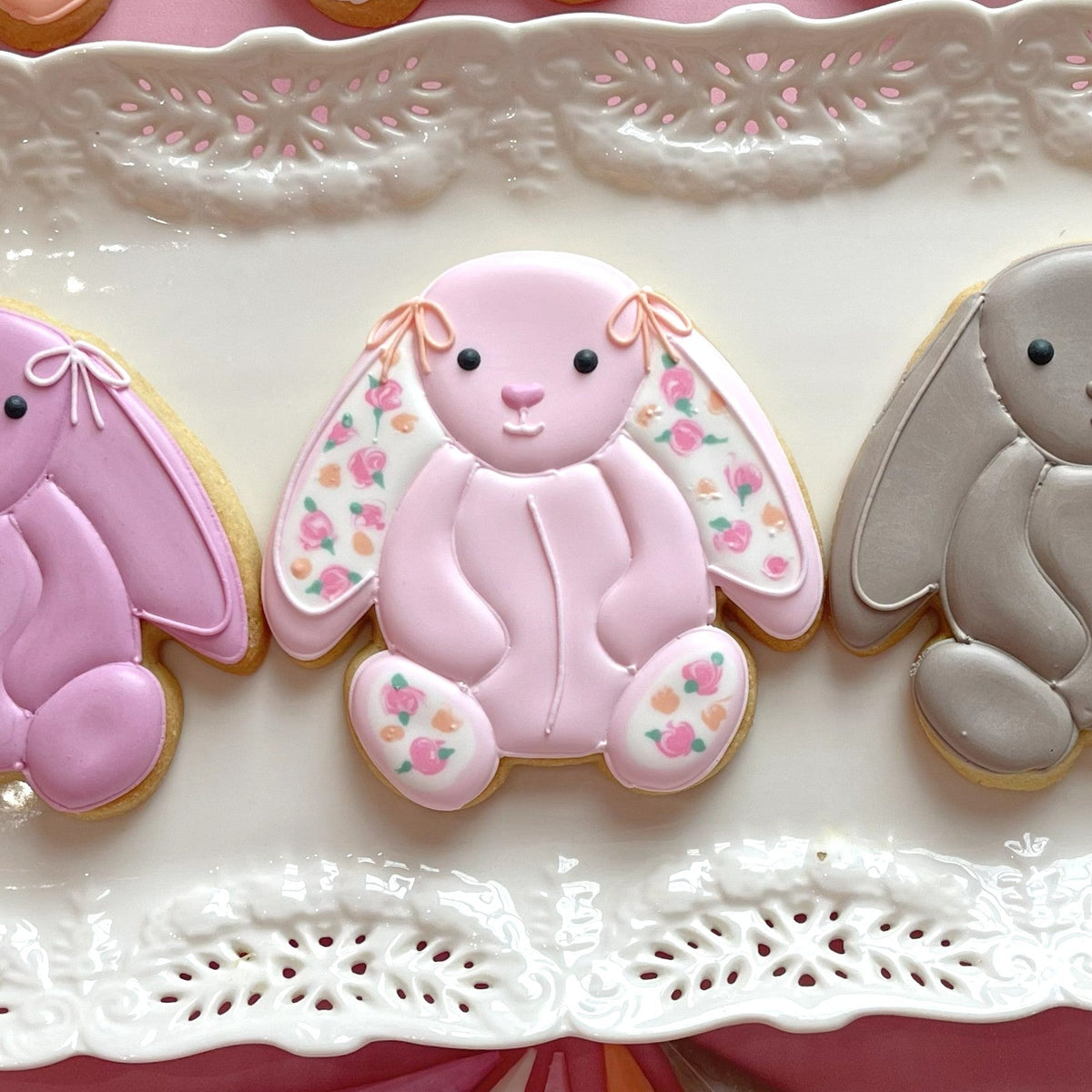 A delicate pink sugar cookie shaped like a bunny with floral icing made using a stuffed bunny cookie cutter