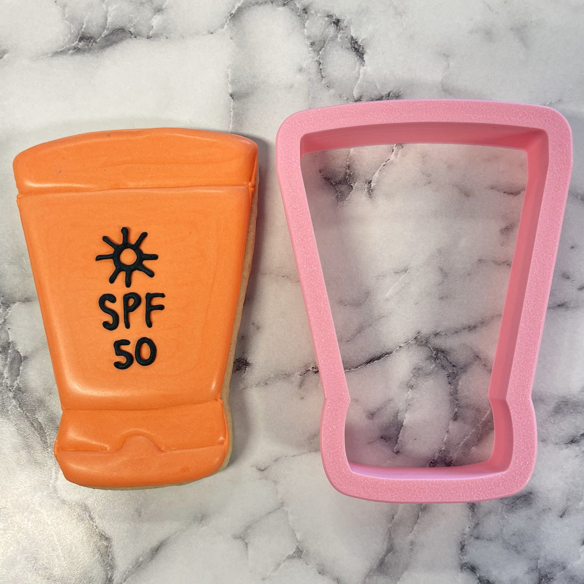 Orange cookie shaped like an spf 50 sunscreen bottle with black icing details made using sunscreen cookie cutter