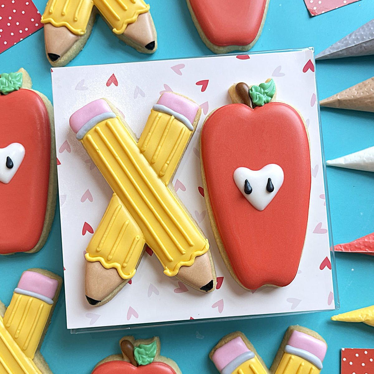 Red apple-shaped cookie with white icing heart face and green leafy top from teacher xo cookie cutter set