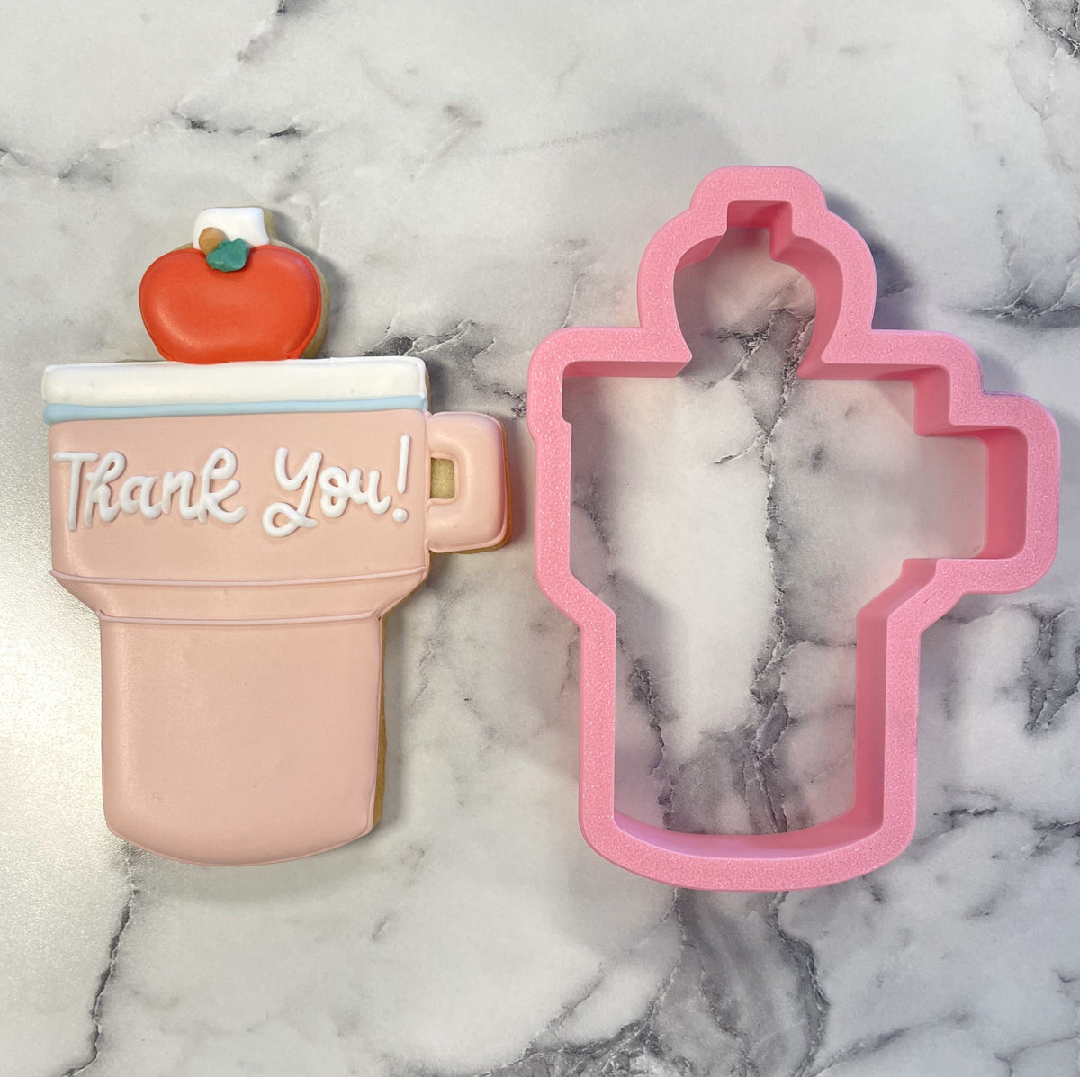 Pink teacher tumbler cookie cutter shaped like a coffee mug with an apple and thank you in white icing