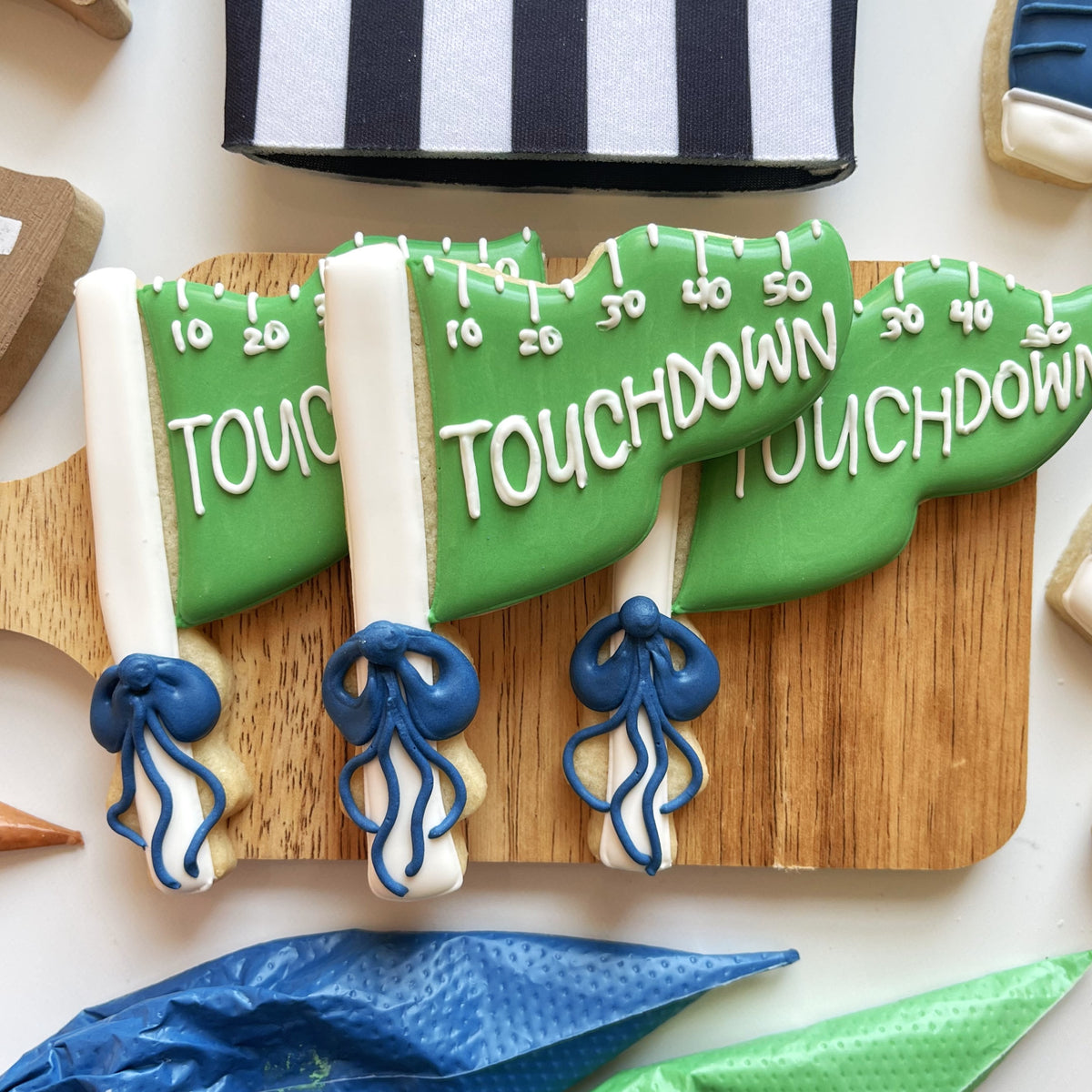 Green and white football touchdown flag shaped cookies with blue icing made using a football cookie cutter bundle
