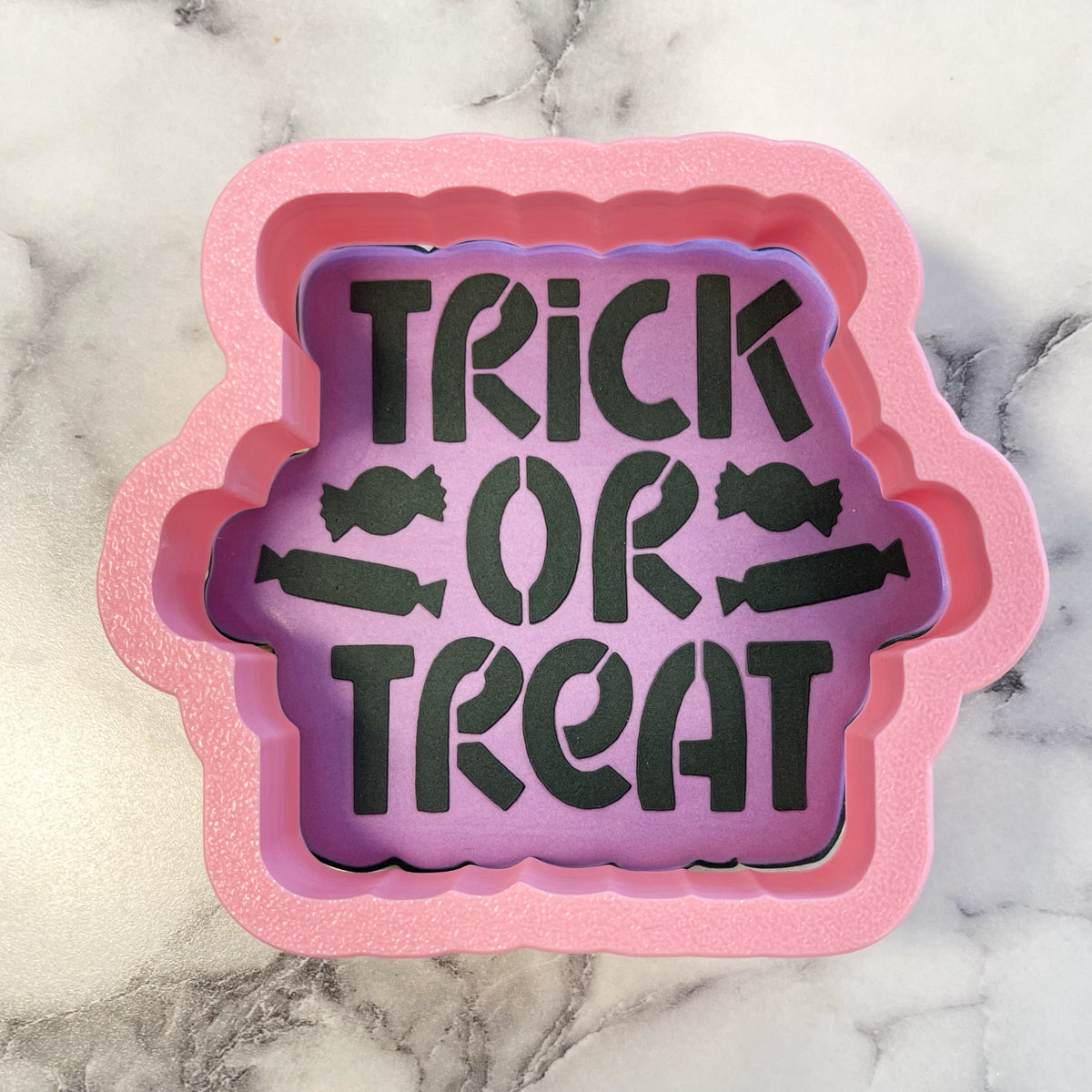 Pink glittery silicone baking mold with purple interior featuring trick or treat design and candy illustrations for cookies