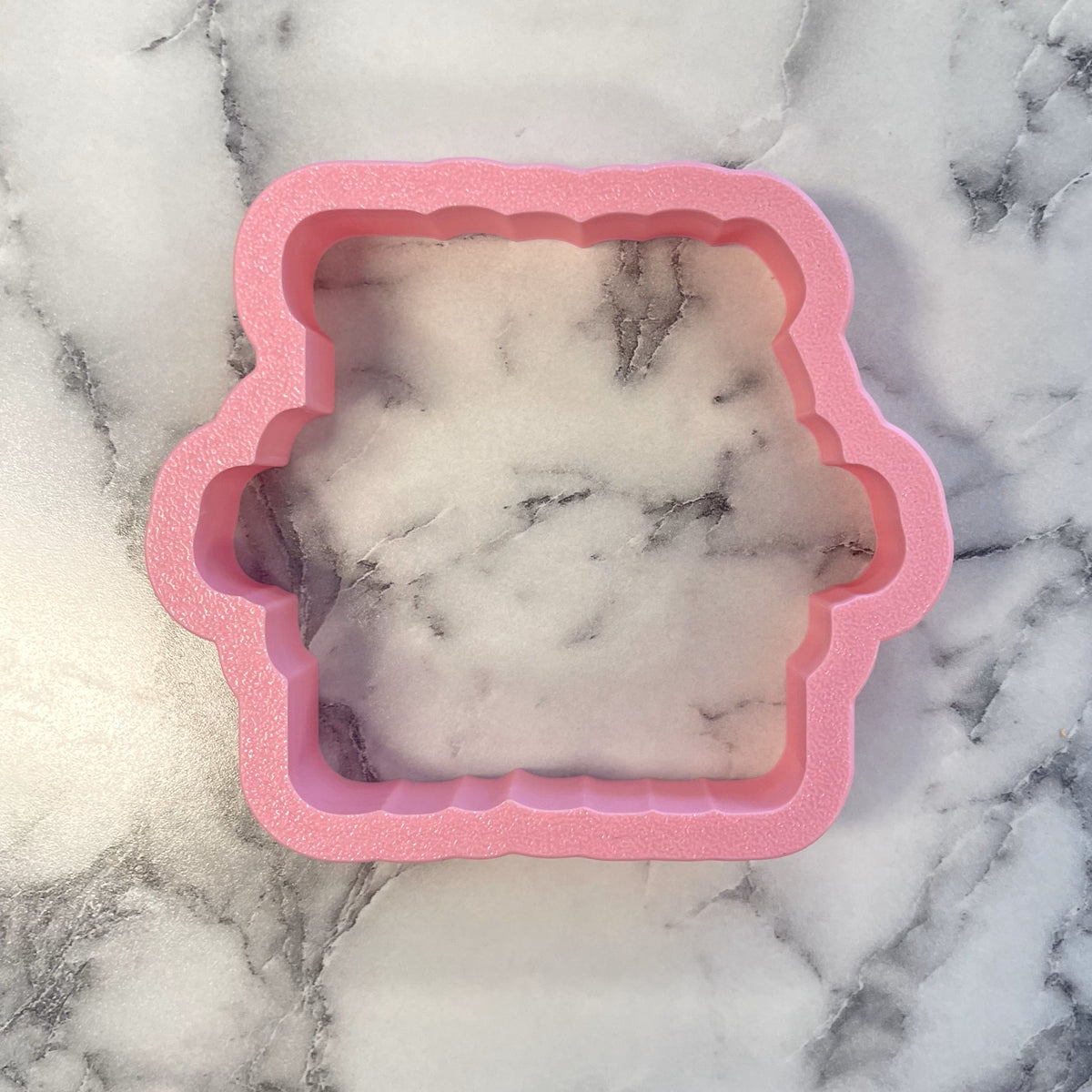 Pink glittery silicone mold with scalloped edge containing white and gray marbled resin for trick or treat plaque cookie cutter