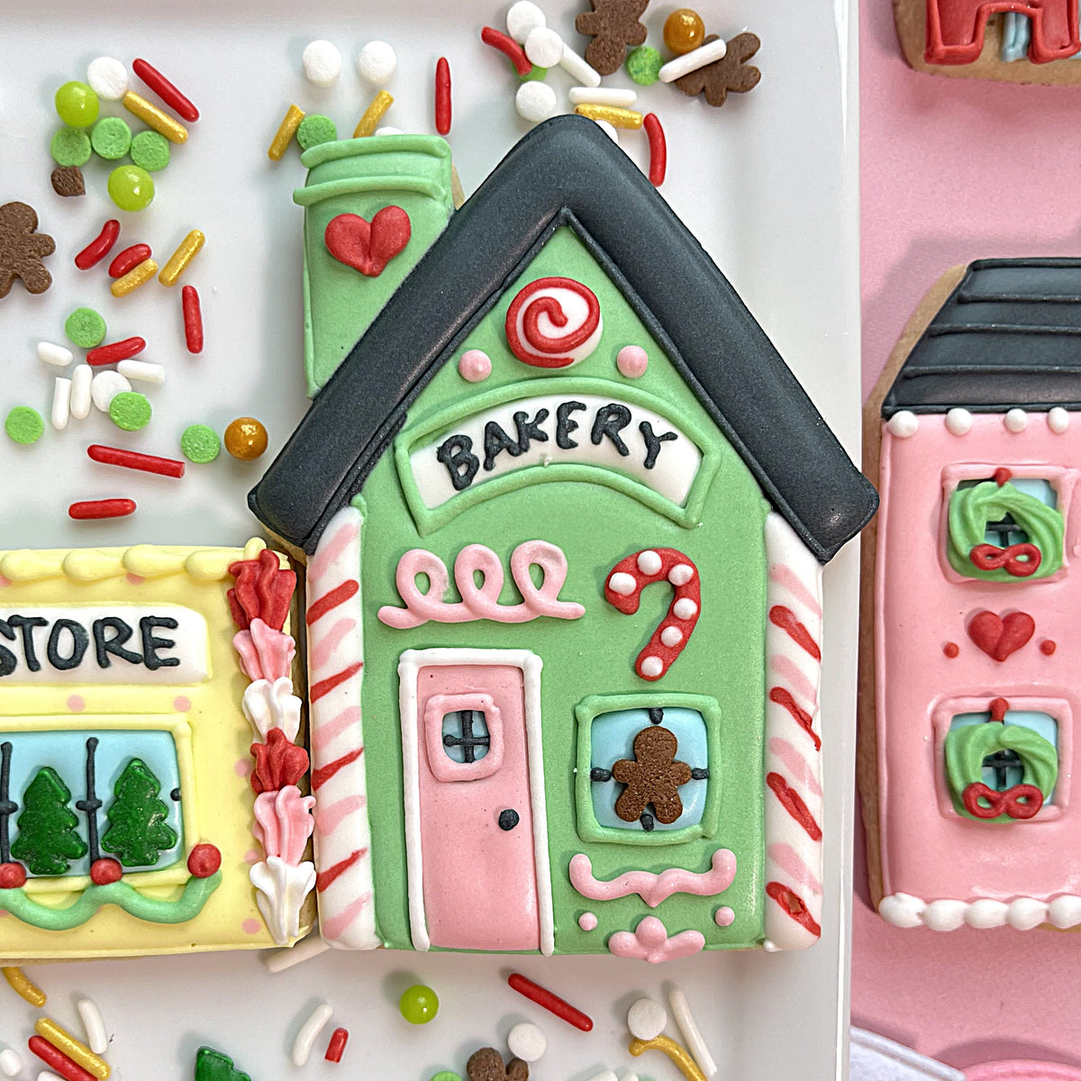 A festive green gingerbread cookie with black roof pink door and candy cane decorations from christmas village cookie cutter bundle
