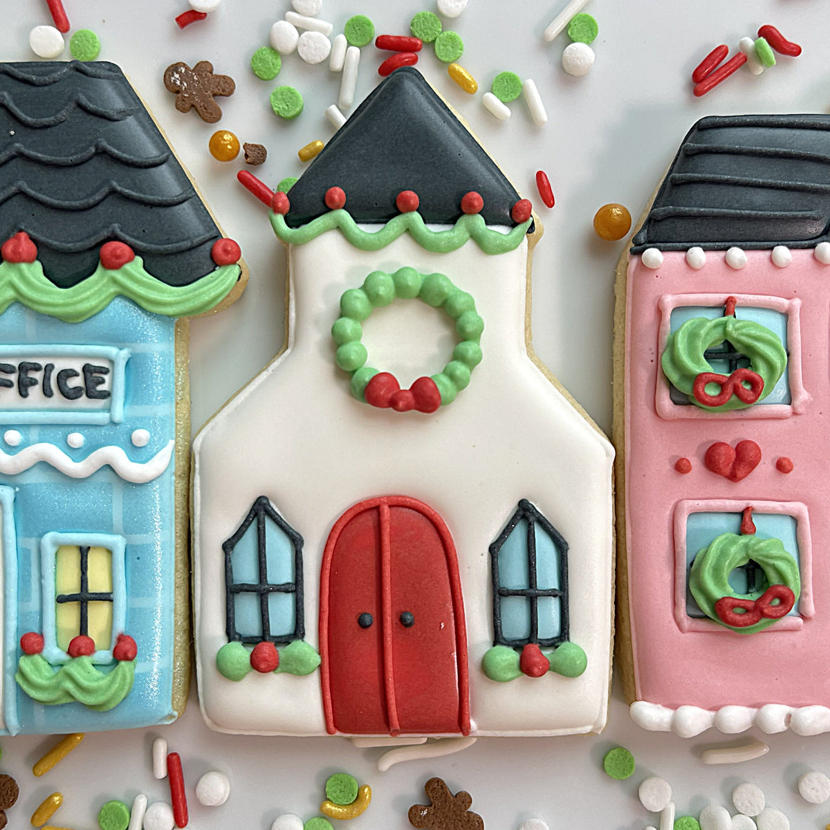 White frosted christmas church cookie with red door green wreath and black roof from christmas village cookie cutter bundle