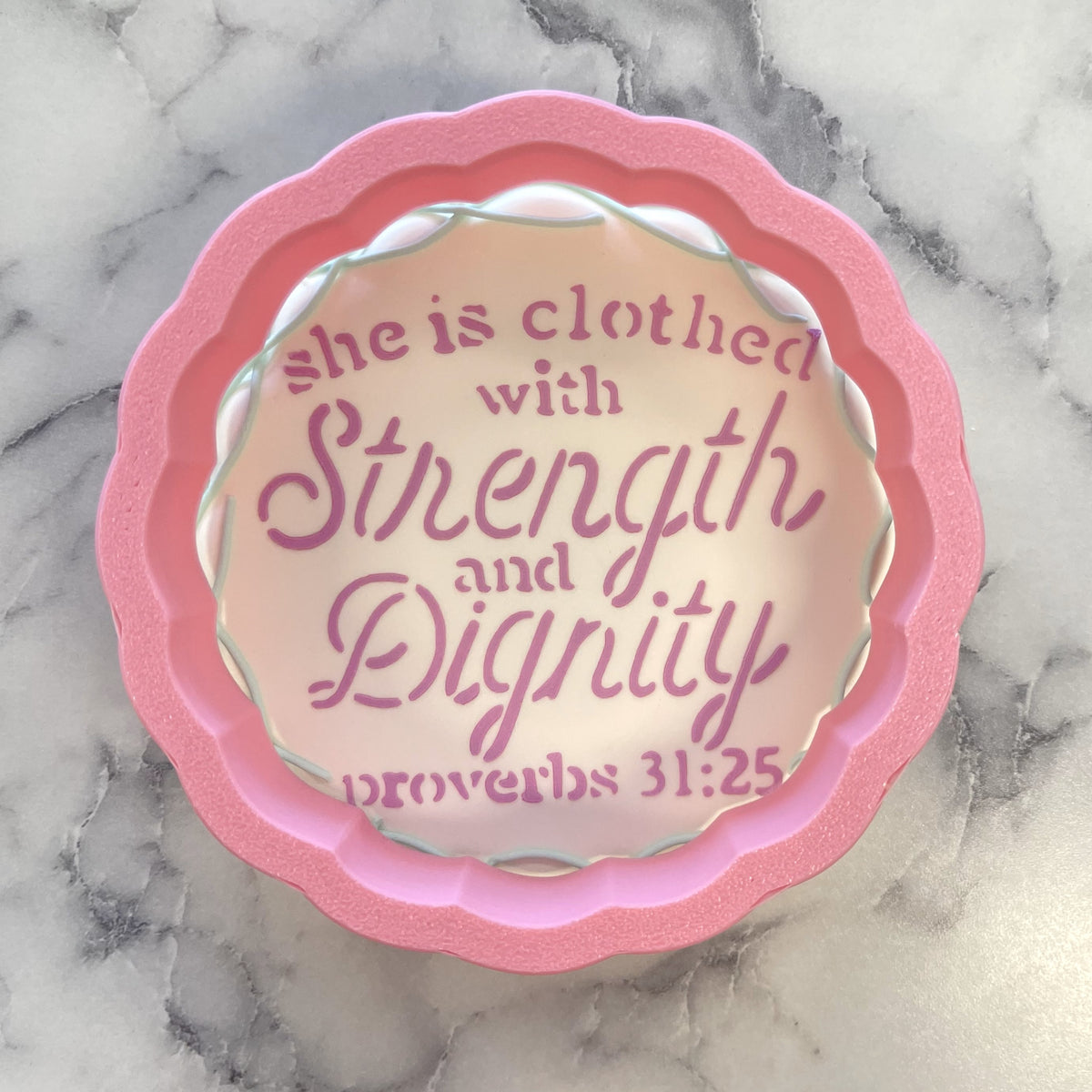 Pink scalloped-edge decorative dish with soft peach center inscribed she is clothed with strength and dignity proverbs 31 25
