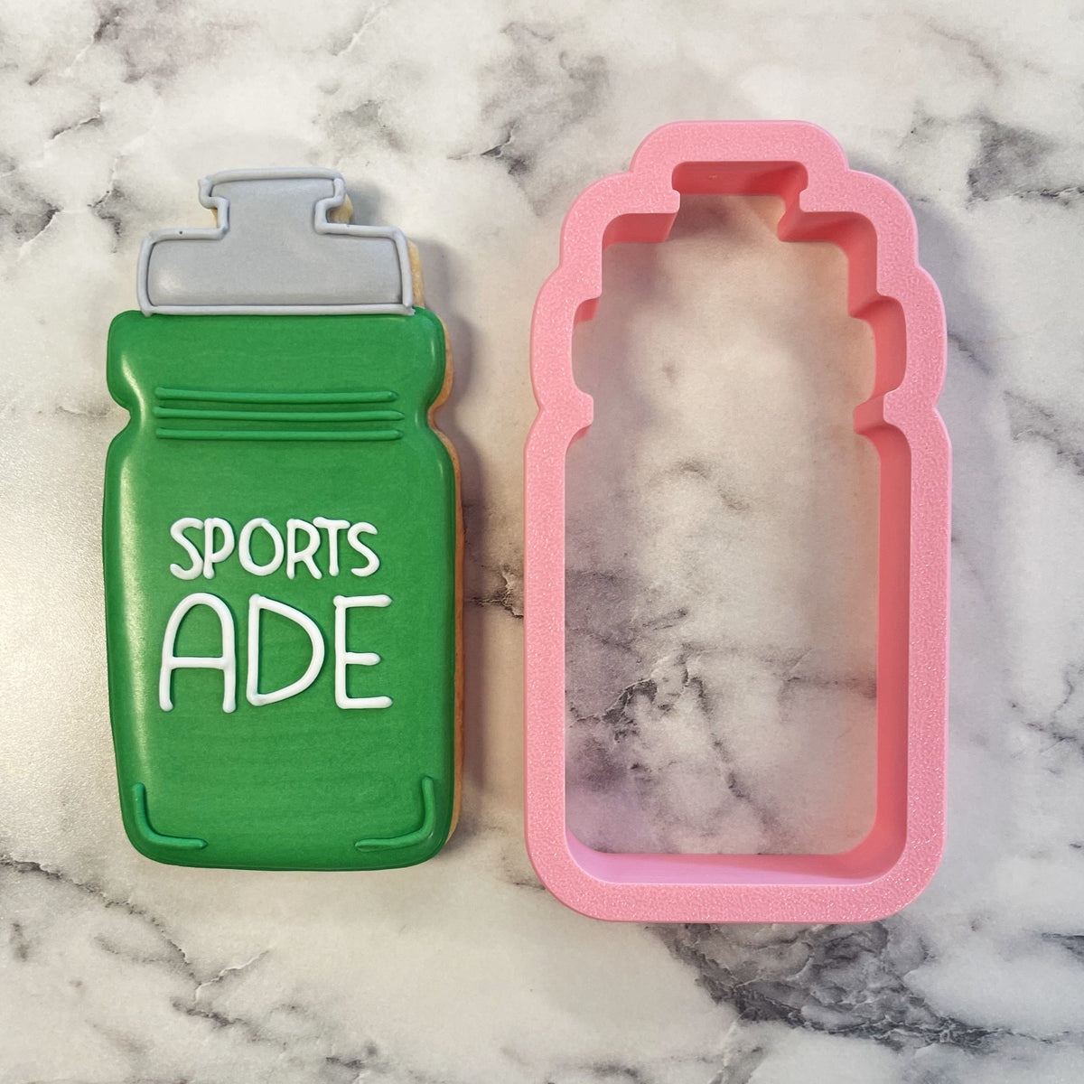 Green sports water bottle cookie next to pink silicone mold of sport water bottle cookie cutter