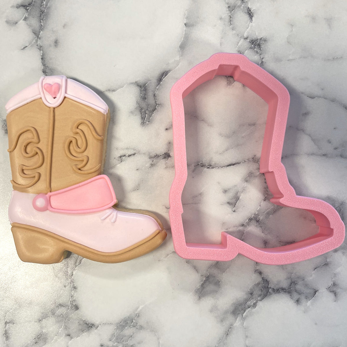 Pink silicone western boot cookie cutter next to a decorated sugar cookie shaped like a matching cowboy boot