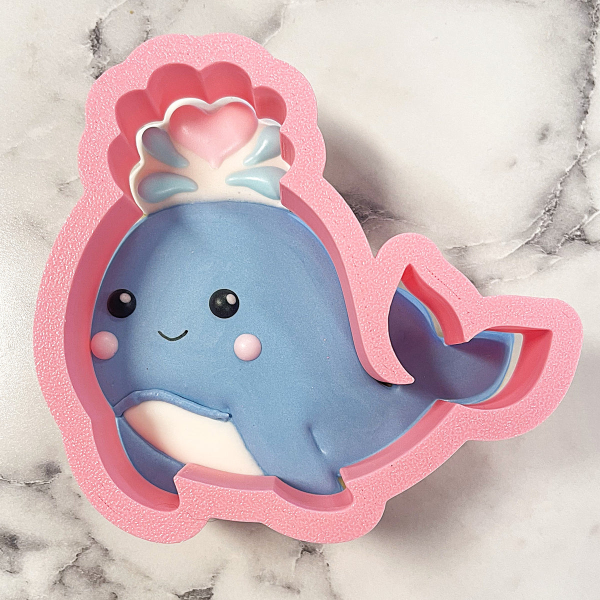Whale with water spray cookie cutter is a pink silicone whale-shaped cutter featuring a blue smiling whale design with a heart shell