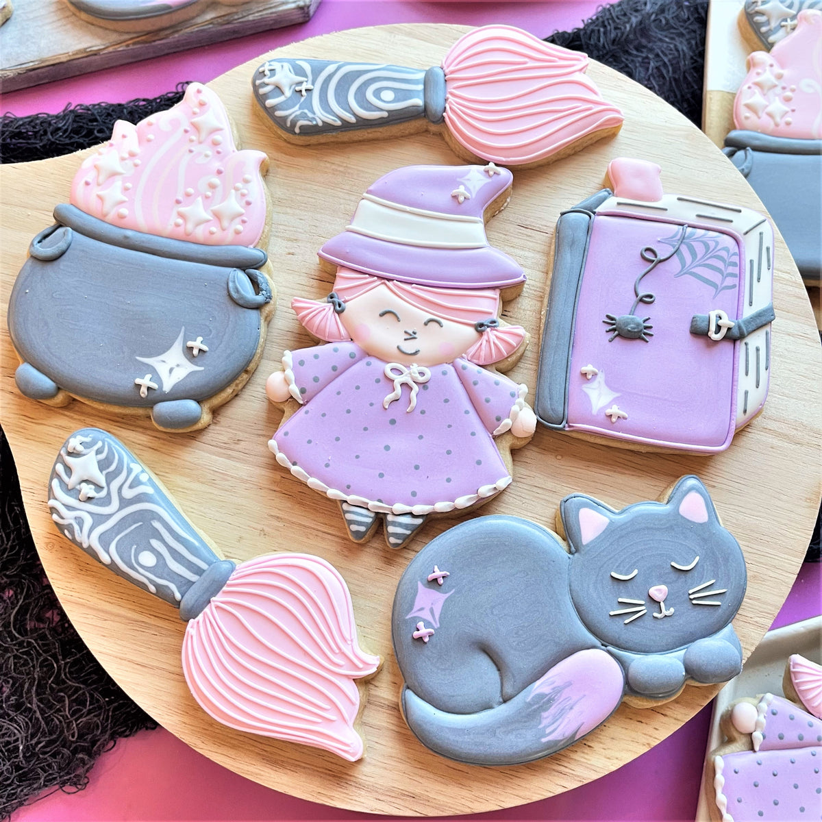 A whimsical purple witch cookie with pink hair wearing a polka-dotted dress and striped leggings for cauldron cookie cutter