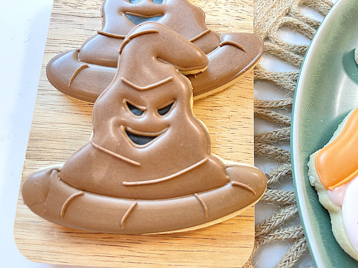 Chocolate-covered sugar cookie shaped like a smiling sorting hat with dark eyes and stitched details from magical wizard cookie decorating kit