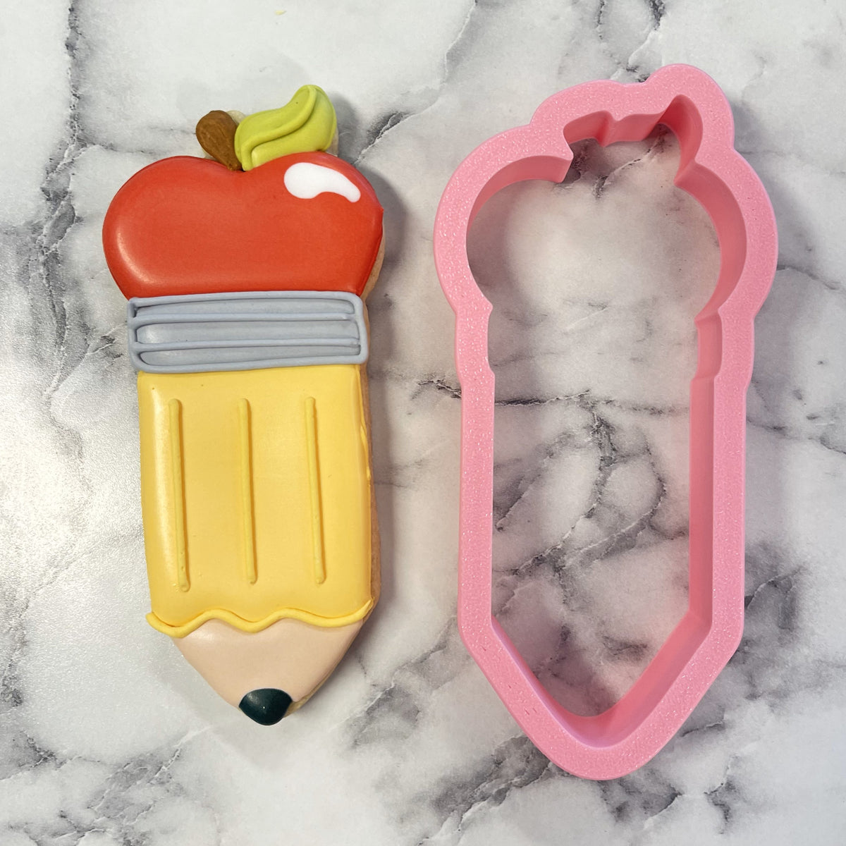 A vibrant red and yellow apple pencil cookie cutter shaped like a pencil with green top, gray band, and black tip
