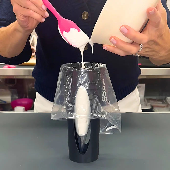 White icing being poured into a clear plastic piping bag fitted over a black piping bag holder from set of 3 bundle