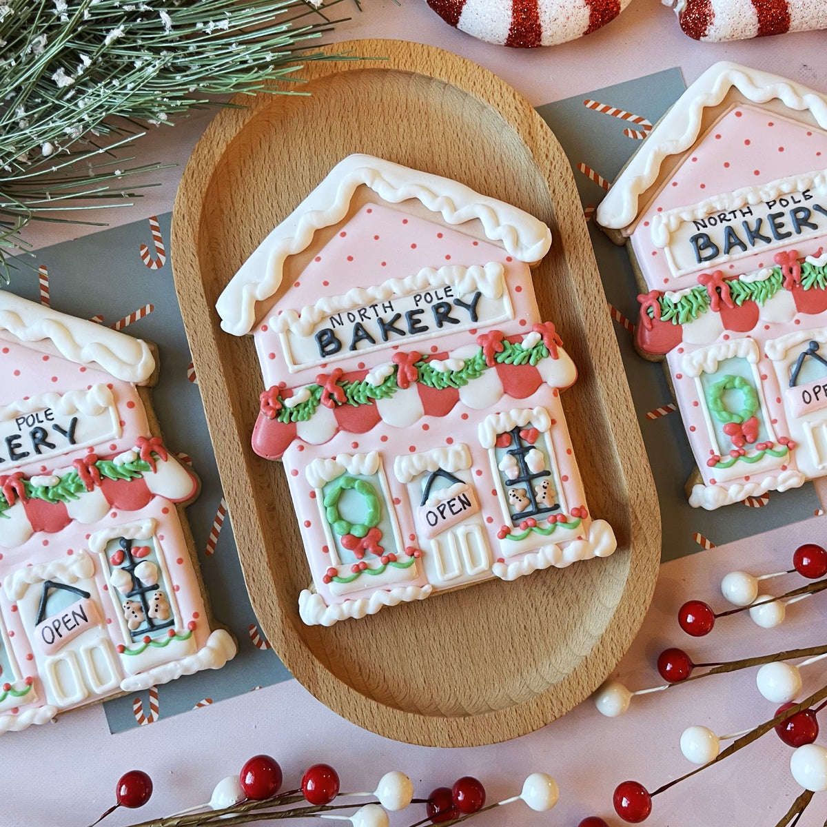 A pink frosted bakery cookie cutter shaped like a gingerbread house with white icing trim green garlands and red accents