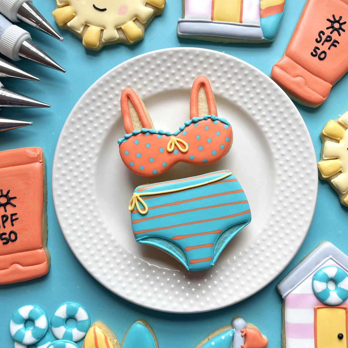 A pair of intricately decorated sugar cookies shaped like a high waist bikini in orange blue polka dots and turquoise coral stripes