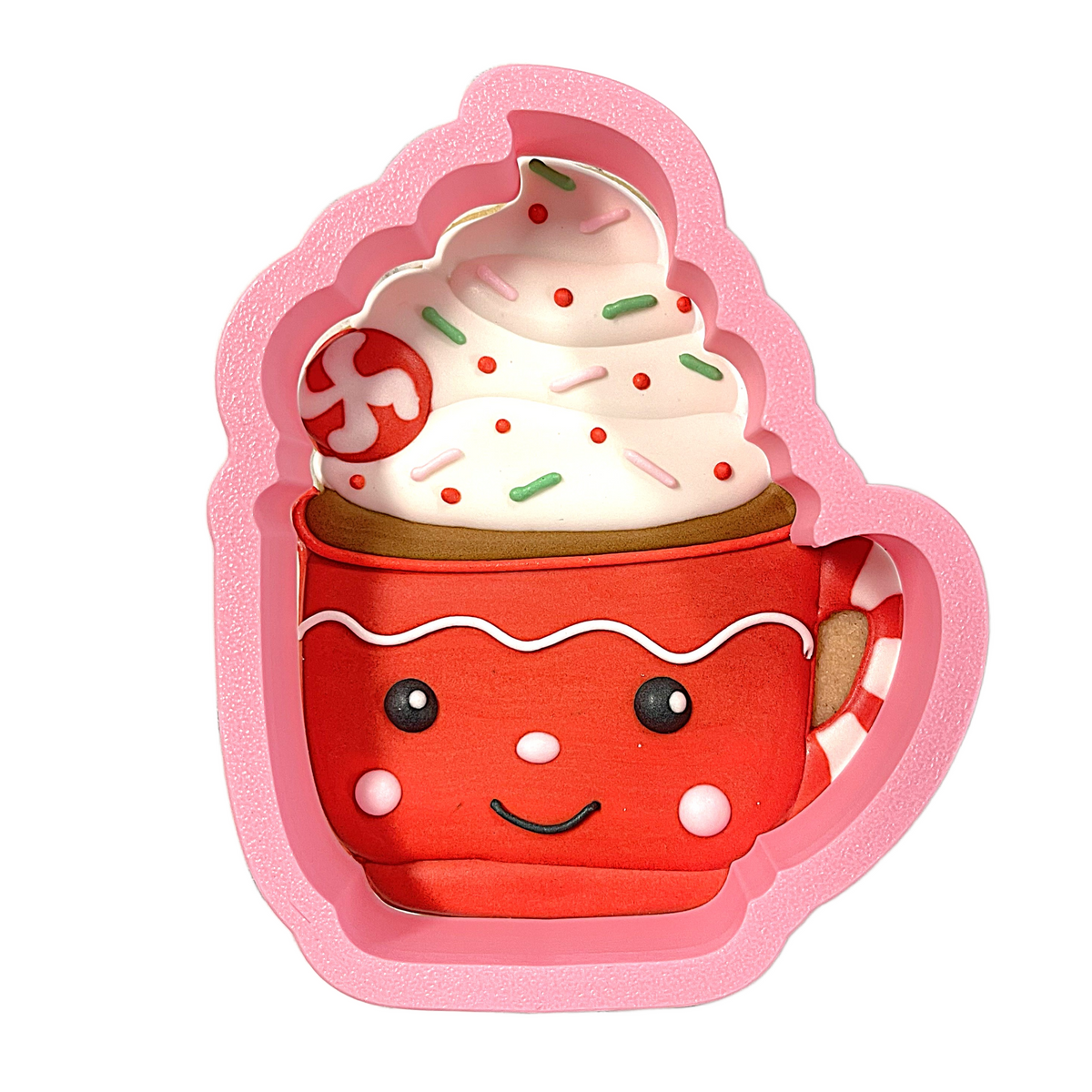 A pink silicone cocoa mug cookie cutter shaped like a smiling red gingerbread filled with whipped cream and sprinkles