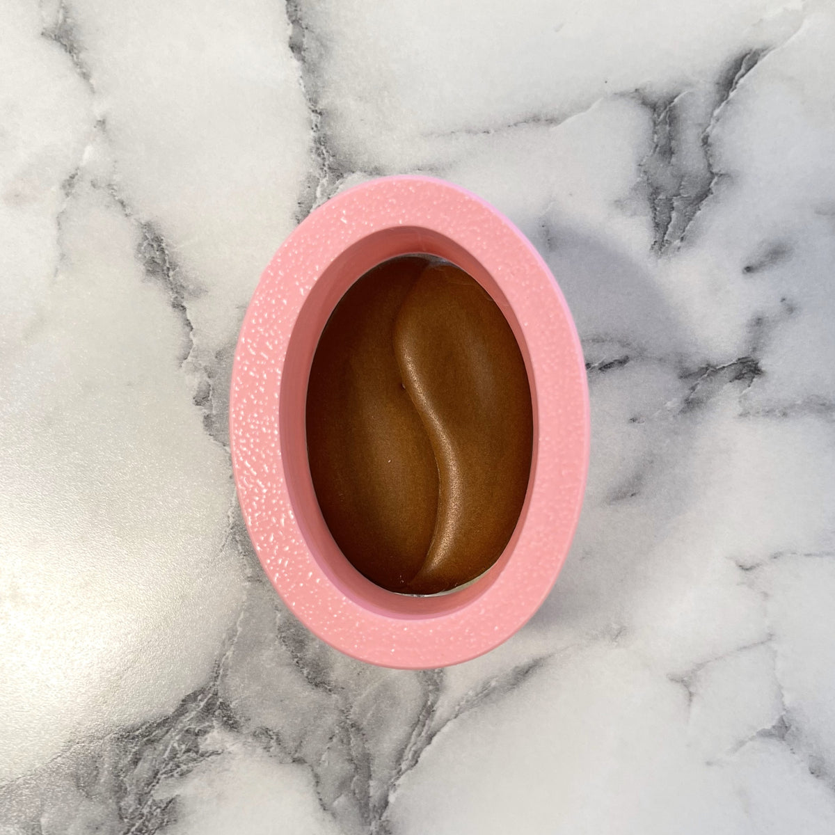 Pink oval-shaped silicone mini coffee bean cookie cutter mold with brown glossy swirling pattern inside