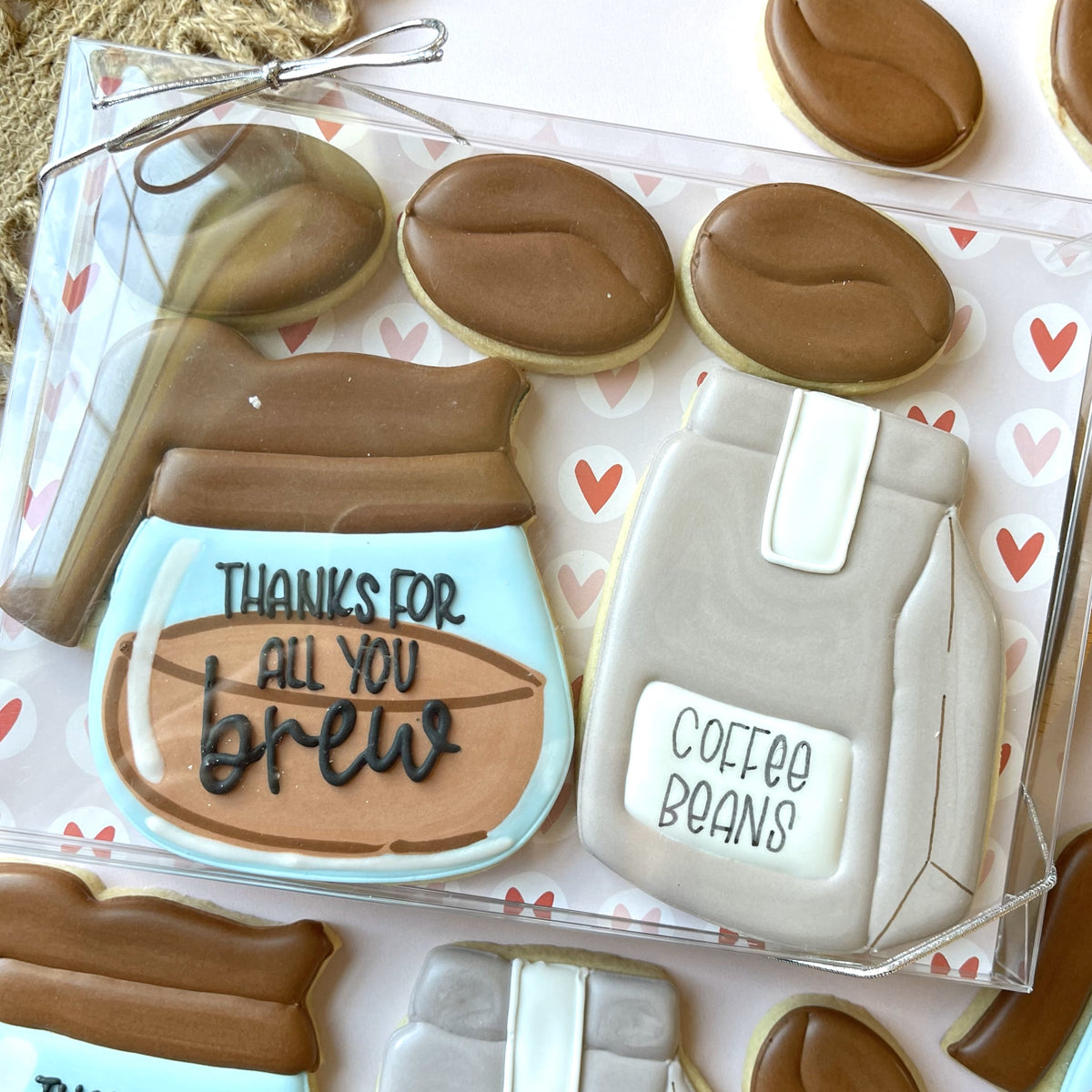 A clear plastic box of intricately decorated coffee-themed sugar cookies frosted in brown and beige tones