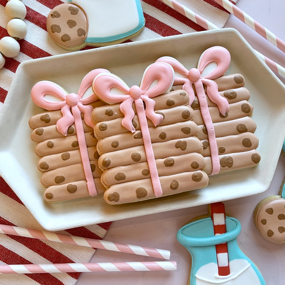 Three gift-shaped cookies with pink icing bows and chocolate chip details made using cookie stack with bow cutter